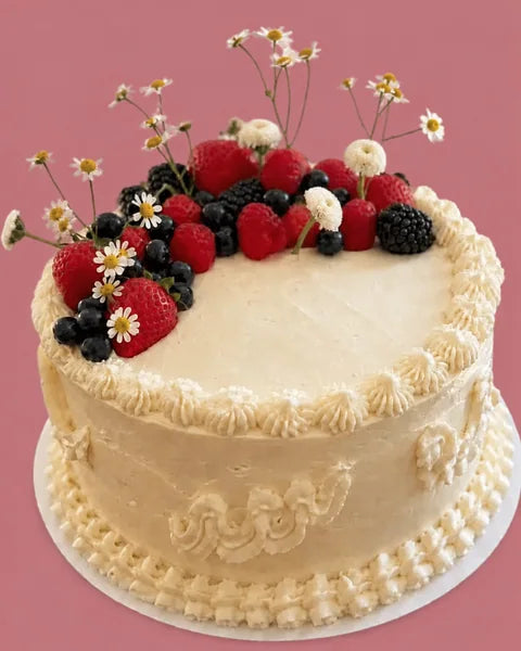 Celebration cake with fresh berries and flowers on a rose background